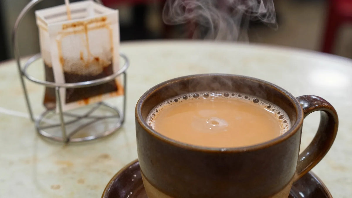 Hong Kong style milk tea in a ceramic cup with a cotton cloth filter sack visible in the background