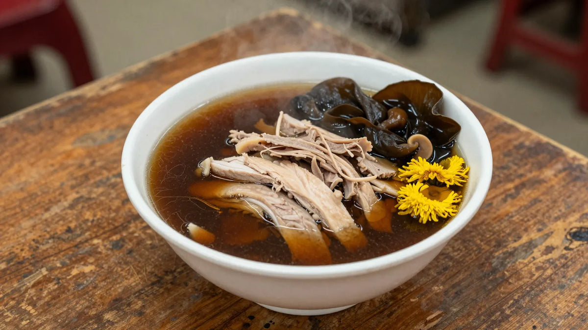 Steaming bowl of Cantonese snake soup with shredded chicken, wood ear mushroom, and chrysanthemum garnish