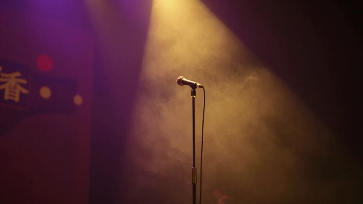A single microphone on an empty stage under a warm spotlight through purple haze, suggesting a vintage Hong Kong concert hall