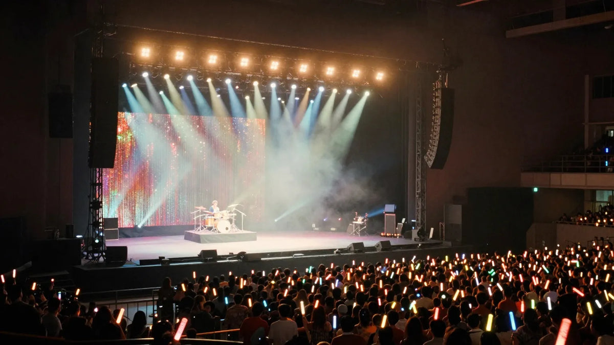 Hong Kong Coliseum concert stage with spotlights and glowsticks in crowd