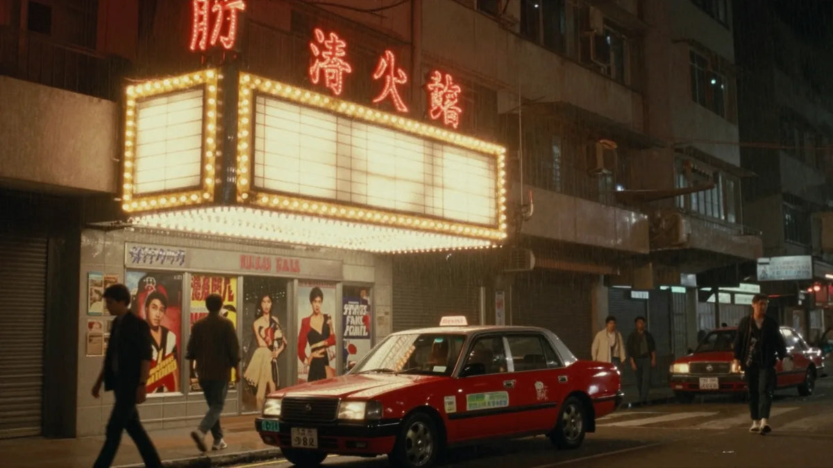 Vintage Hong Kong cinema marquee at night with glowing bulbs and film posters, parked red taxi in the rain