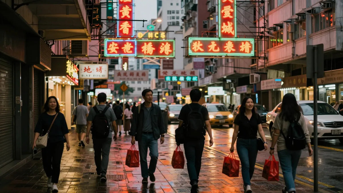 Dense Hong Kong street at dusk with neon signs and pedestrians carrying shopping bags walking home from work
