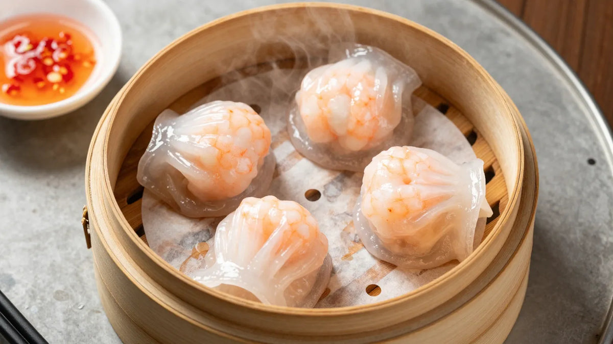 Four crystal shrimp har gow dumplings in bamboo steamer with chili oil