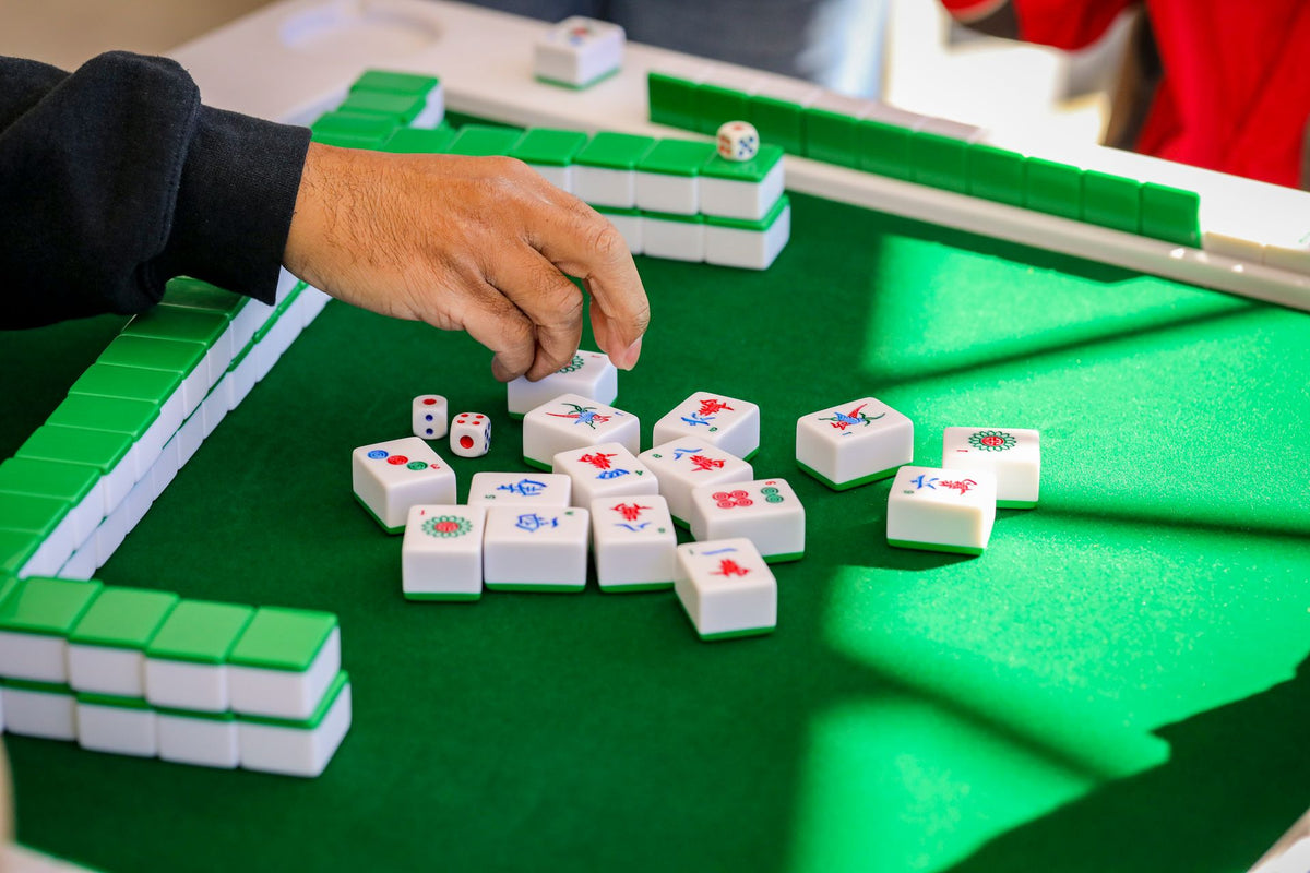 A hand arranging mahjong tiles during a game on a green felt table