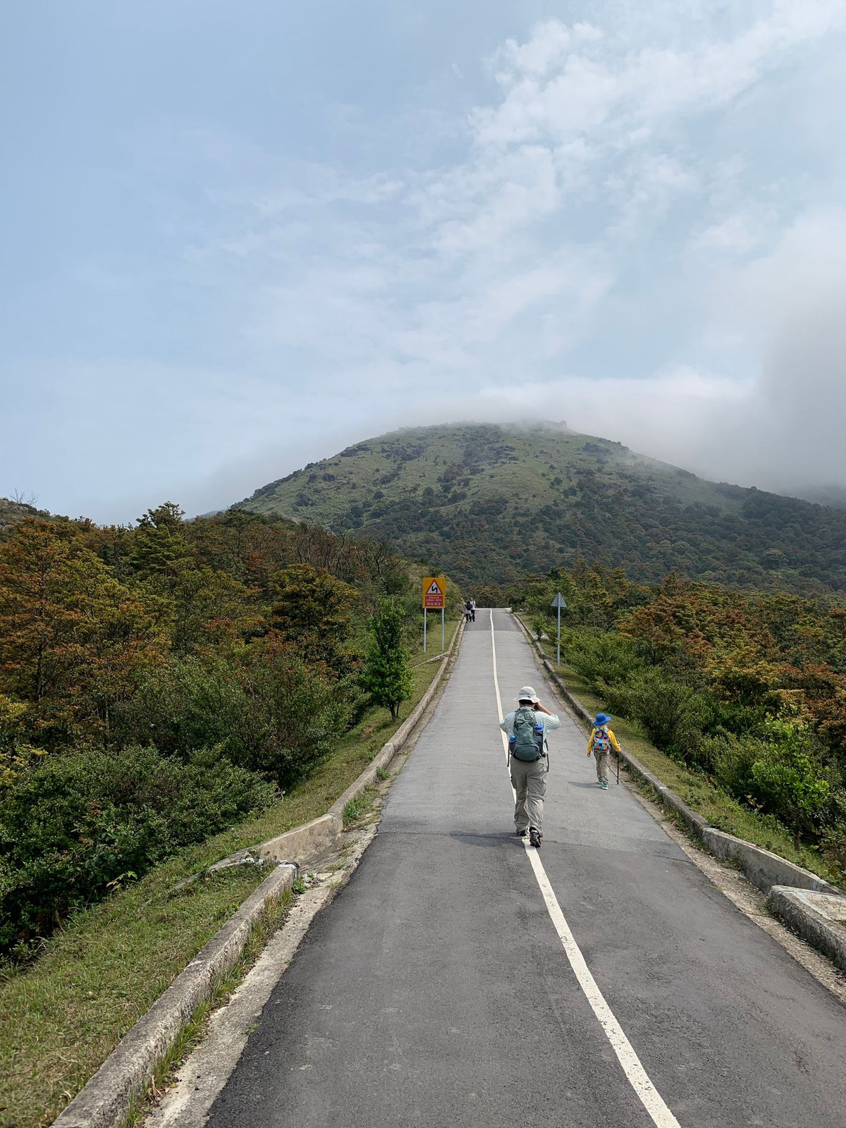 Hiker walking on a scenic mountain road in Hong Kong, representing the Lion Rock Spirit of climbing on
