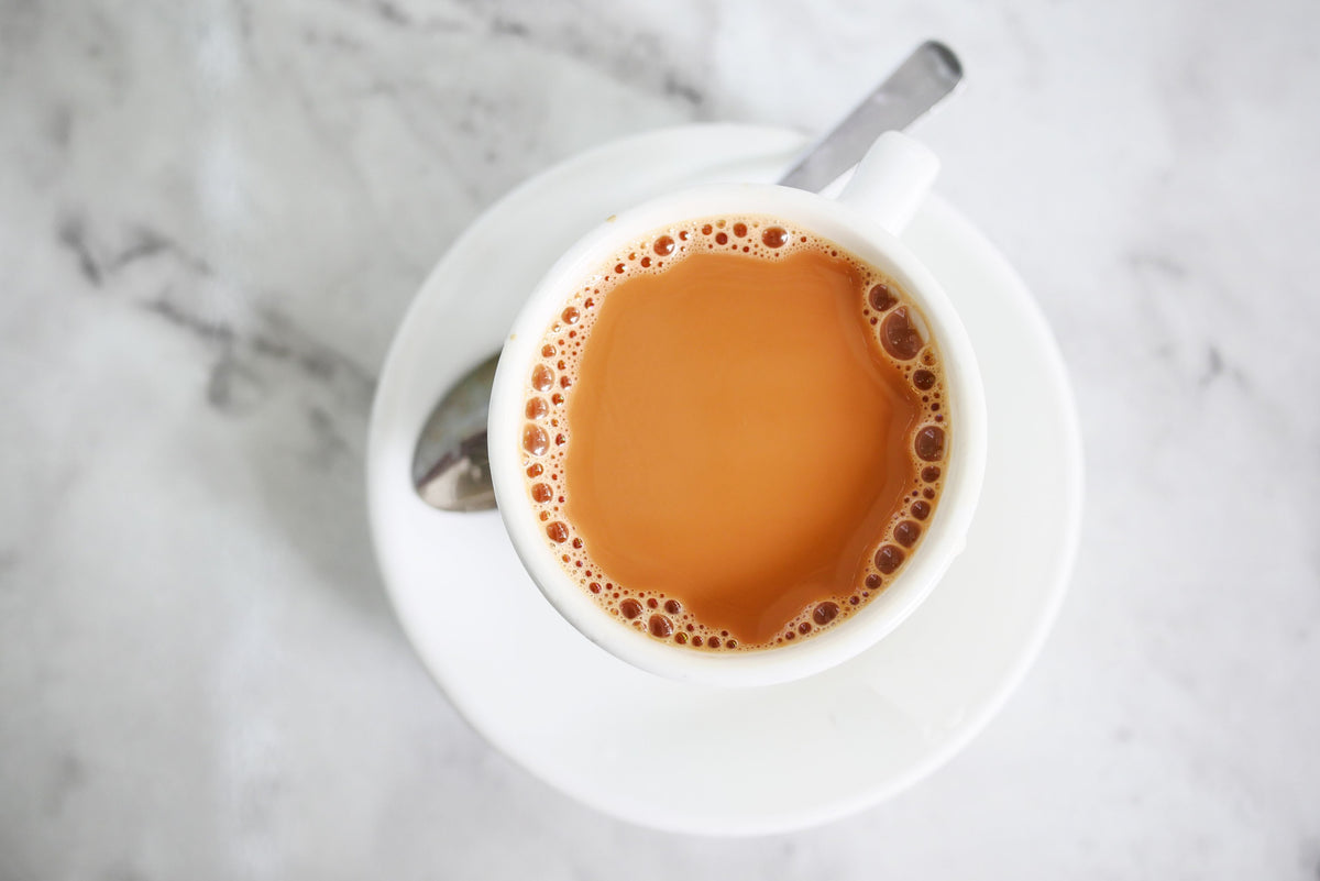 Close-up of a steaming cup of coffee-tea style drink on a white saucer — Yuenyeung