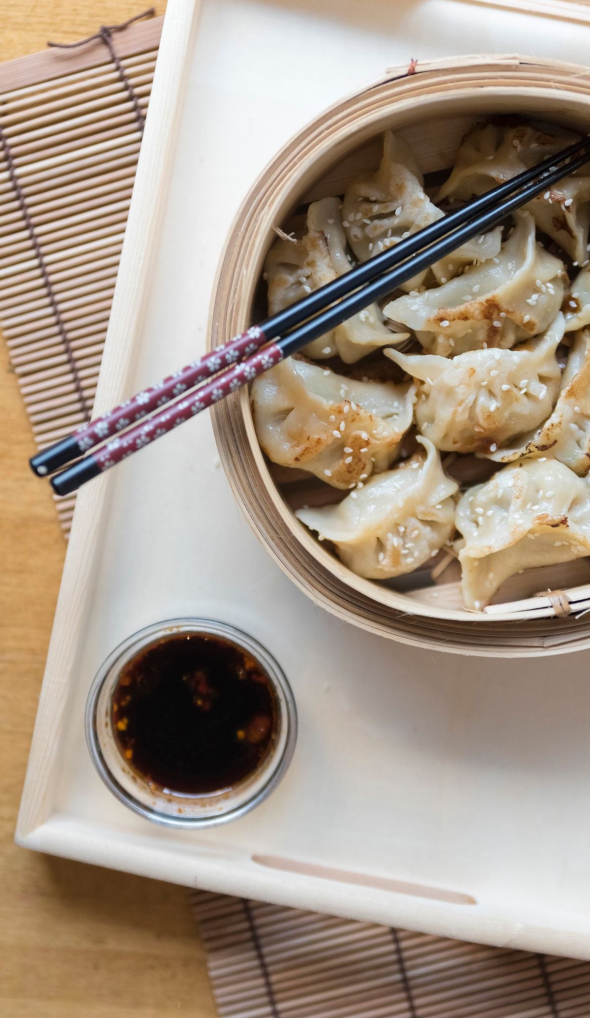 Steamed dumplings served on a bamboo tray with chopsticks and soy sauce