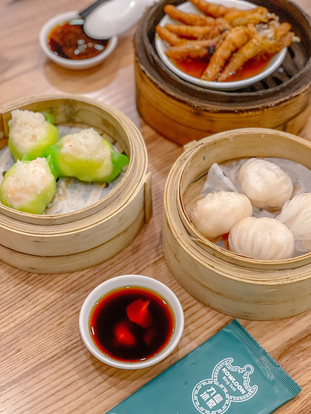 Assorted Cantonese dim sum dumplings in bamboo steamers with dipping sauces on a wooden table