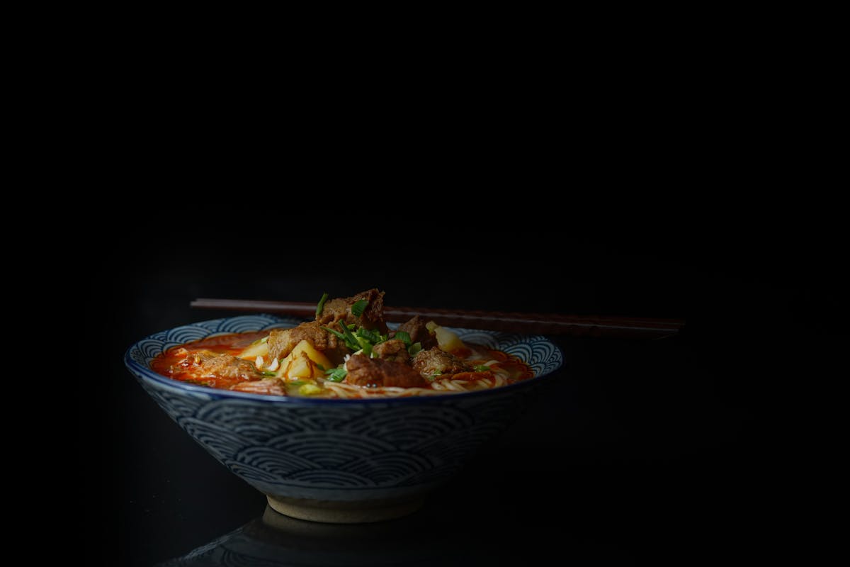 Bowl of Asian noodle soup with garnishes on a dark background