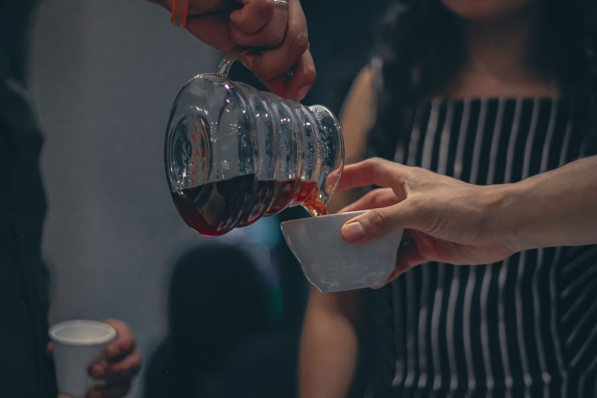 Close-up of hands pouring hot tea from a teapot into a small cup