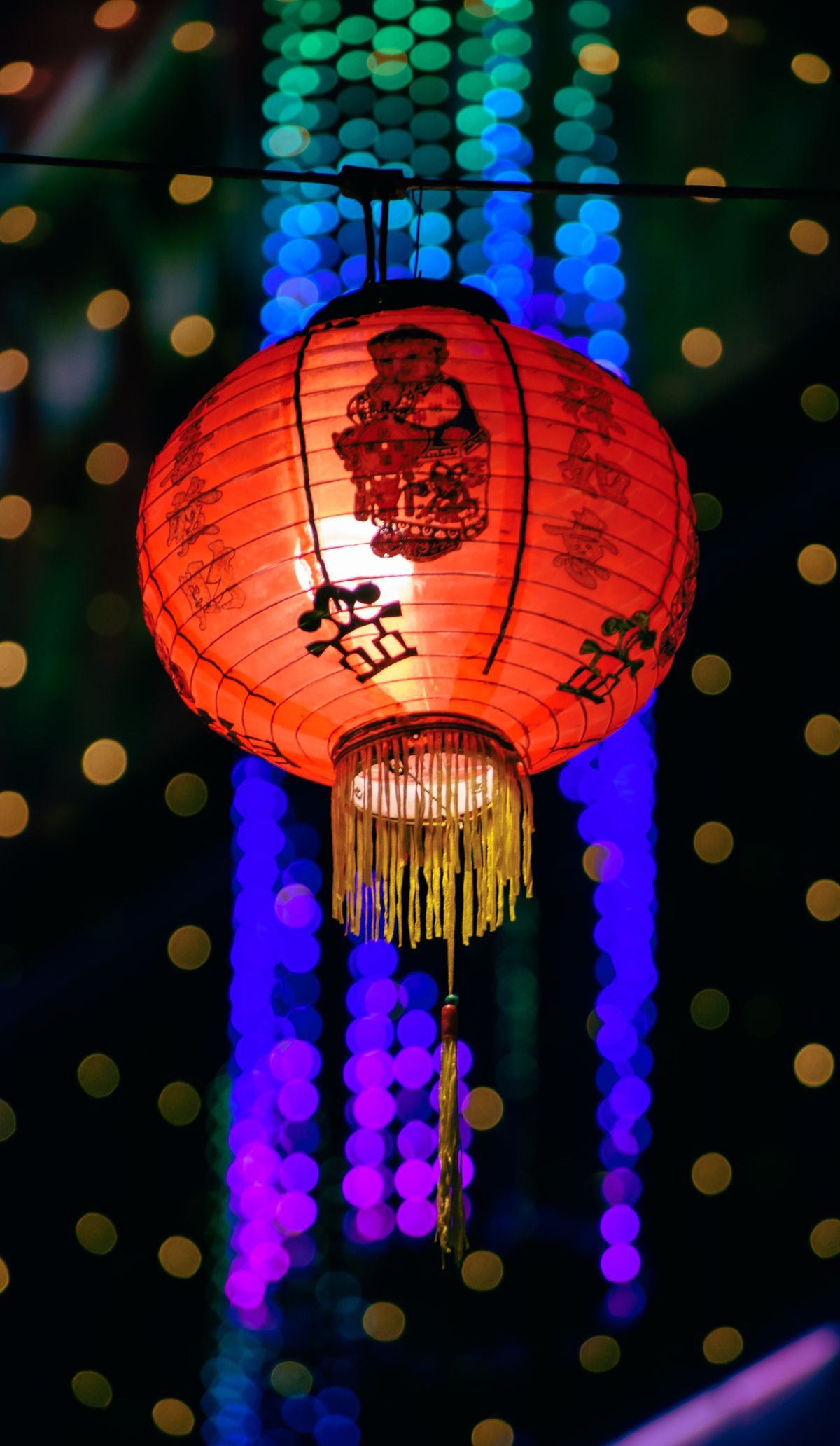A red traditional Chinese lantern glowing at night against a festive backdrop