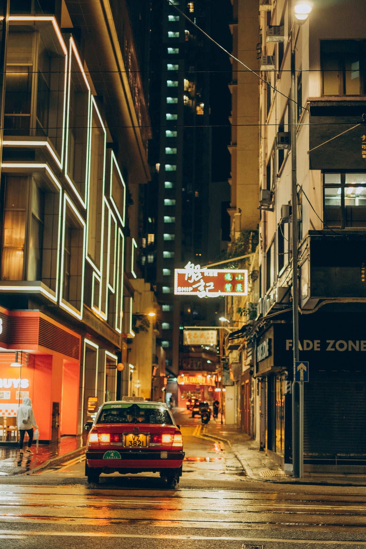 Red taxi driving down a Hong Kong street at night, illuminated by neon signs