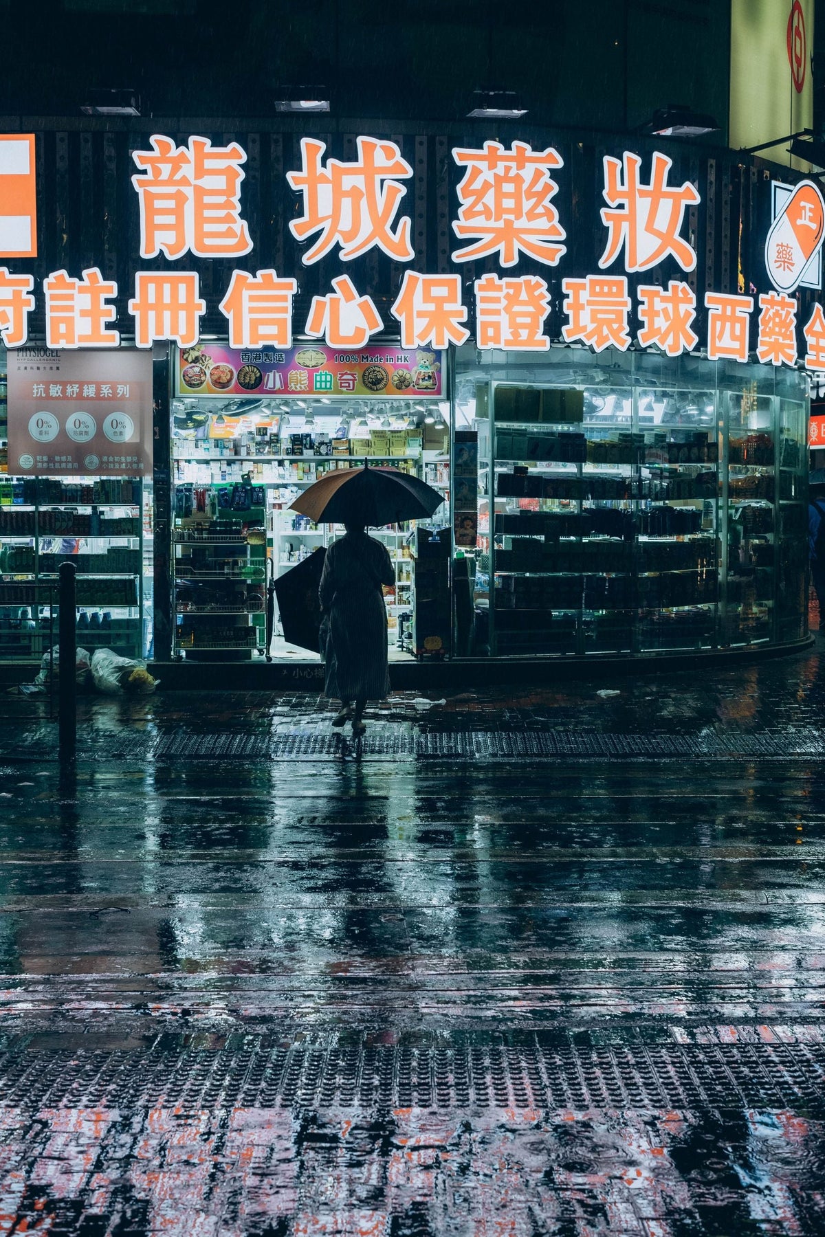 Woman with an umbrella crossing a rainy Hong Kong street at night under glowing shopfront lights