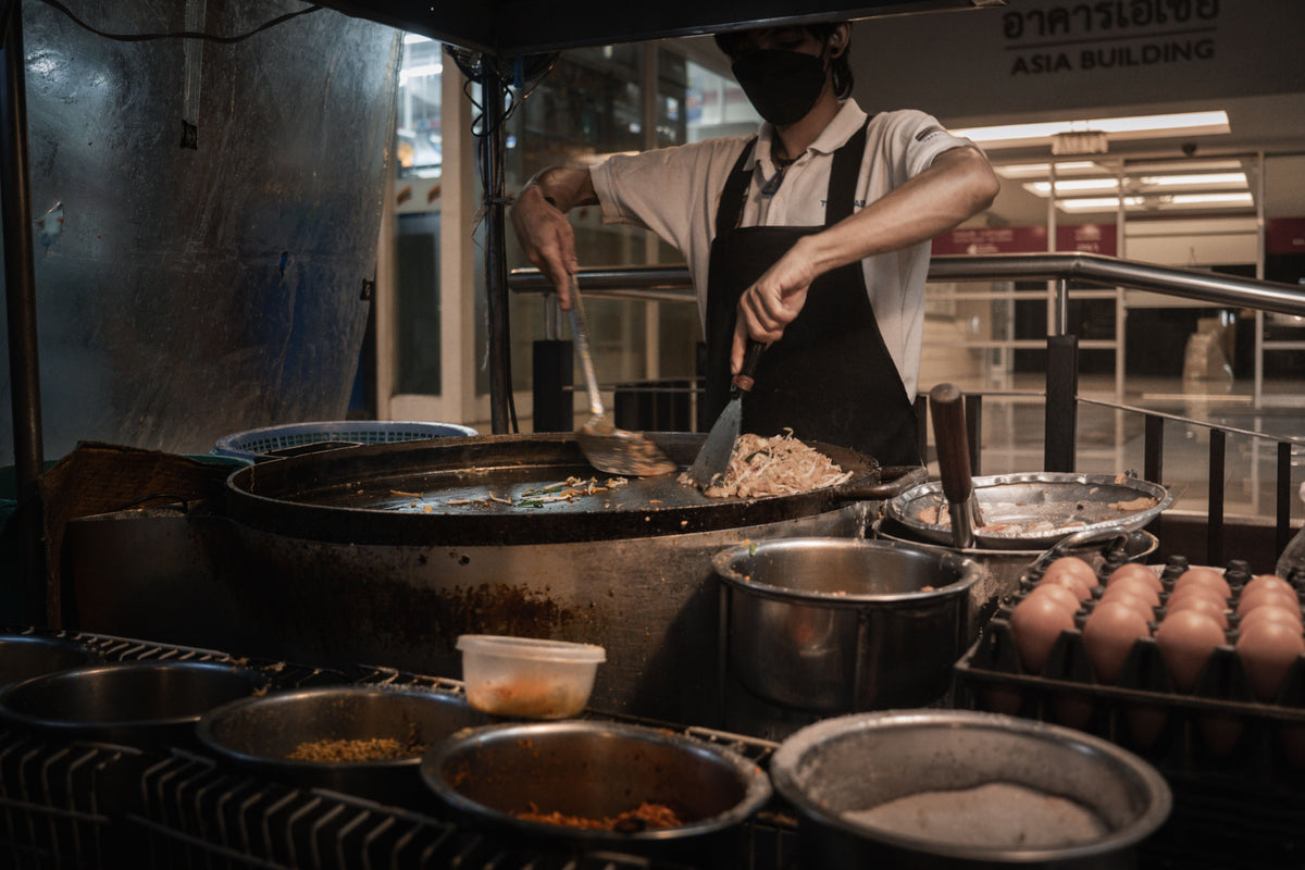 A chef in an Asian night market preparing traditional street food under bright lights