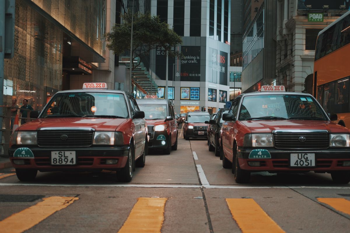 Red Toyota Crown Comfort taxis on a street in Hong Kong, showing the city's iconic red vehicle culture