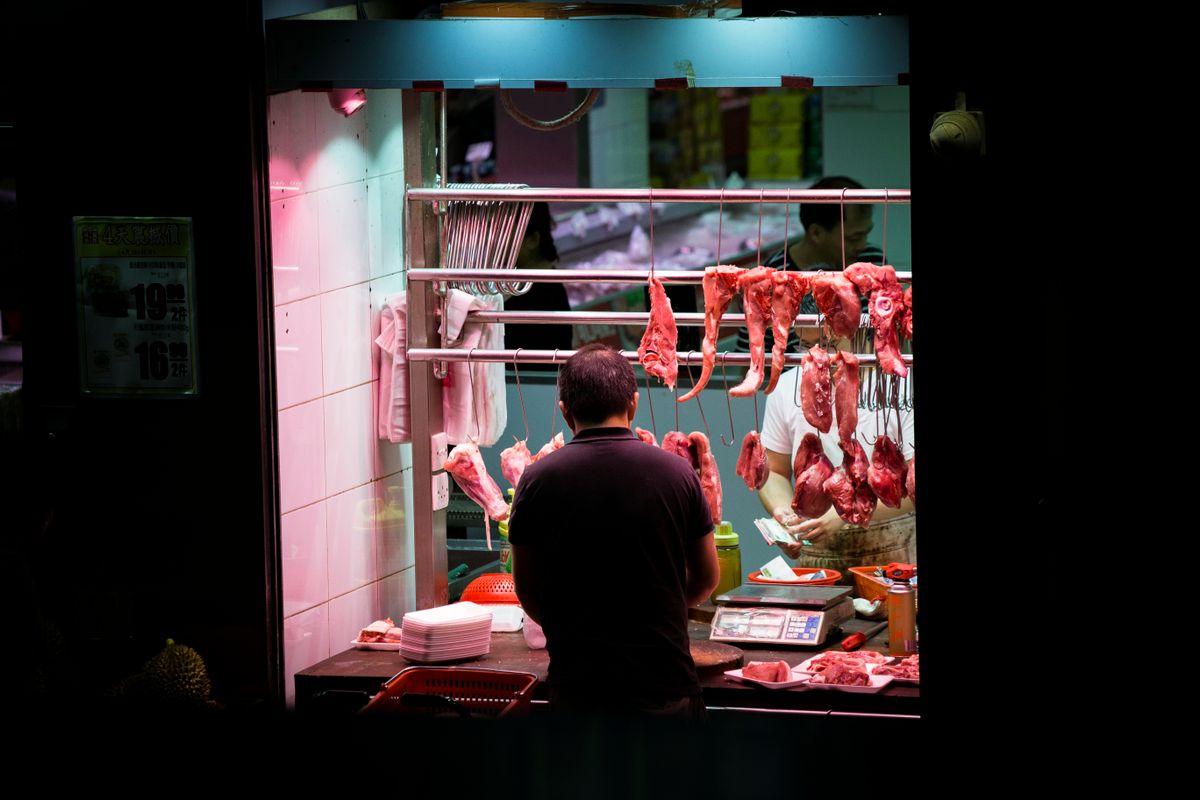 A Hong Kong butcher standing in front of his market stall with hanging roast meats