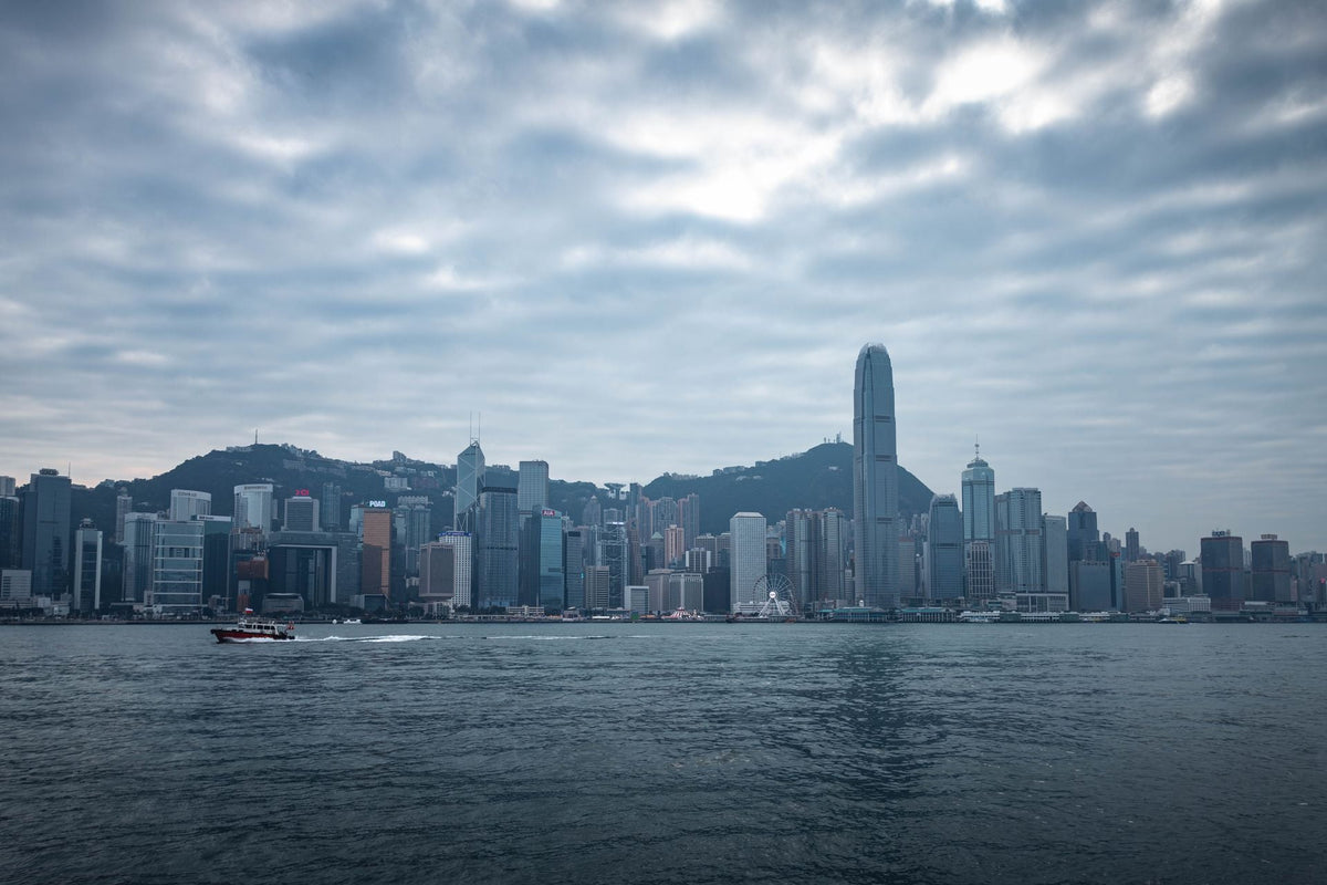 Hong Kong skyline under dramatic cloudy sky reflecting on Victoria Harbour water