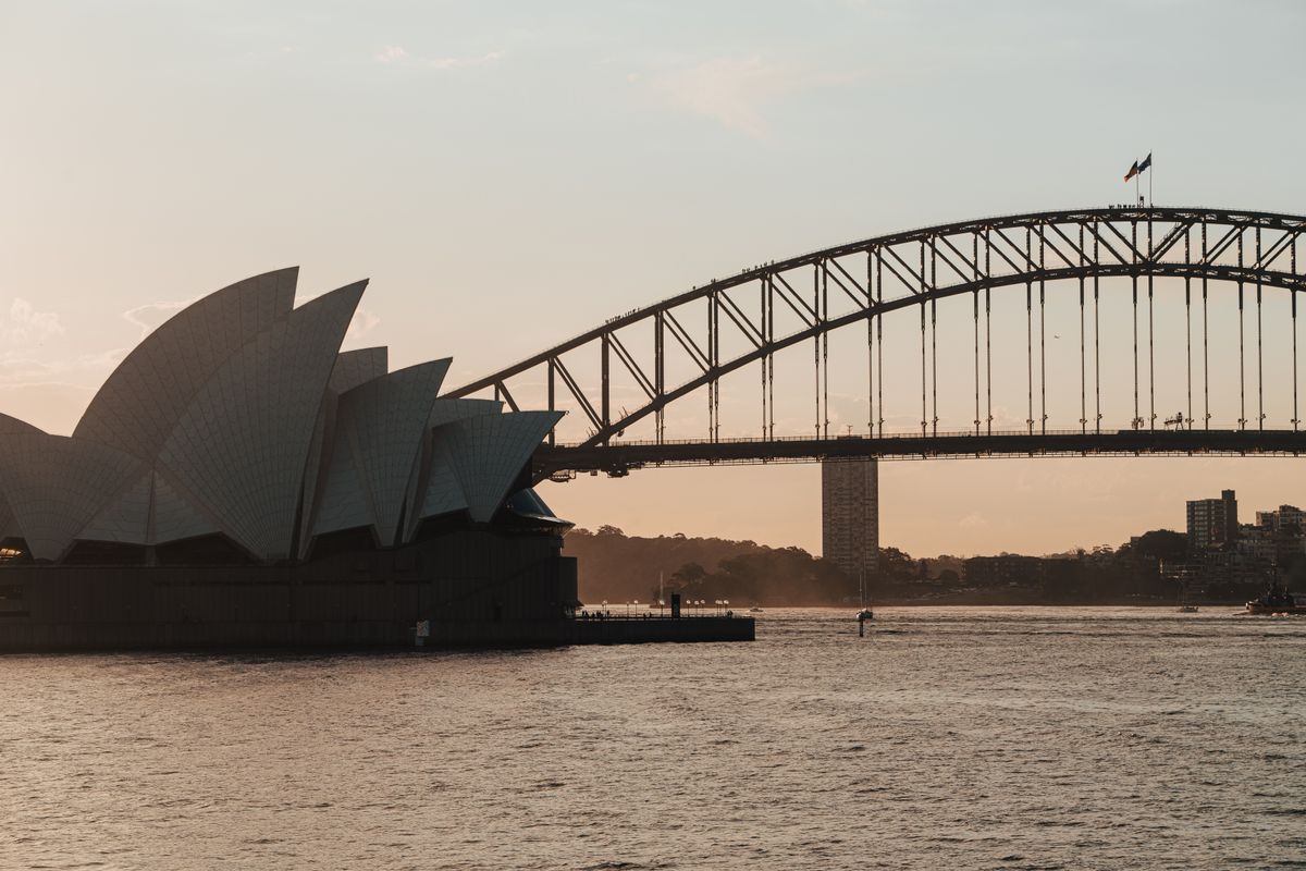 Sydney Harbour Bridge and Sydney Opera House at dusk, viewed across calm water