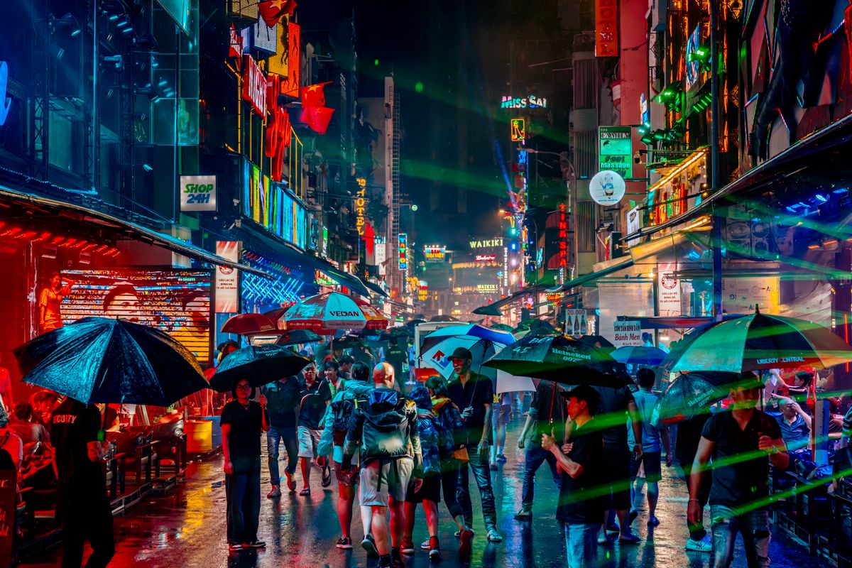 Rainy neon-lit Asian city street with people under umbrellas at night