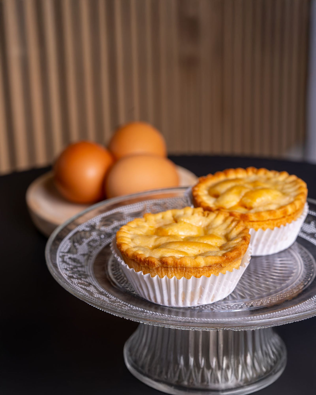 Freshly baked Cantonese egg tarts on a glass stand with eggs in the background