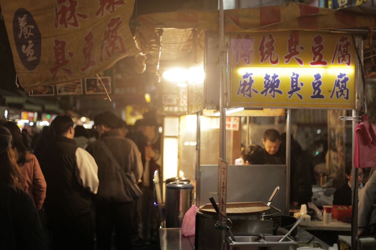 Bustling Asian night market food stall with steaming pots and neon lights