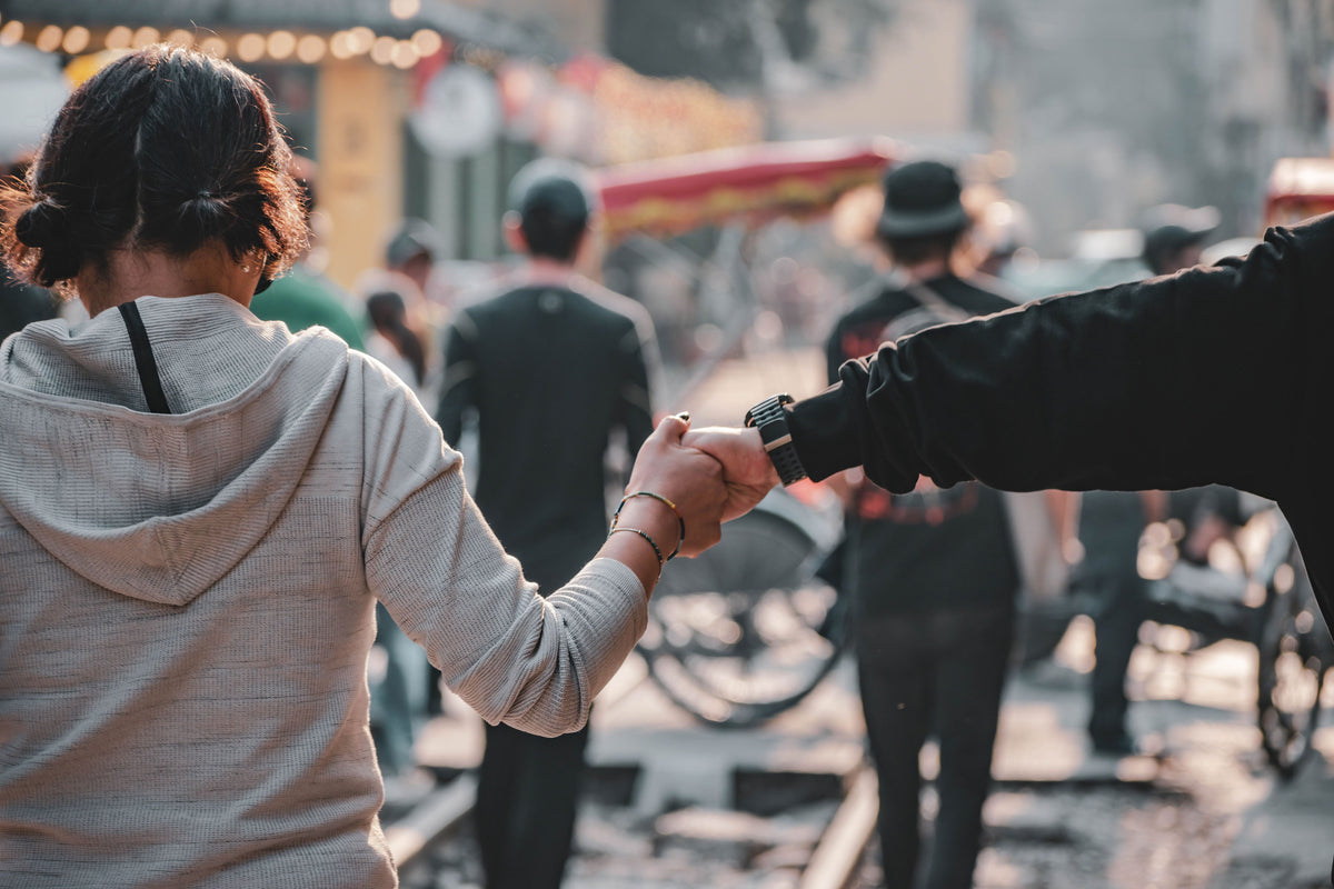 Young couple walking hand in hand on a bustling Asian street at dusk, layered lights reflecting off wet pavement