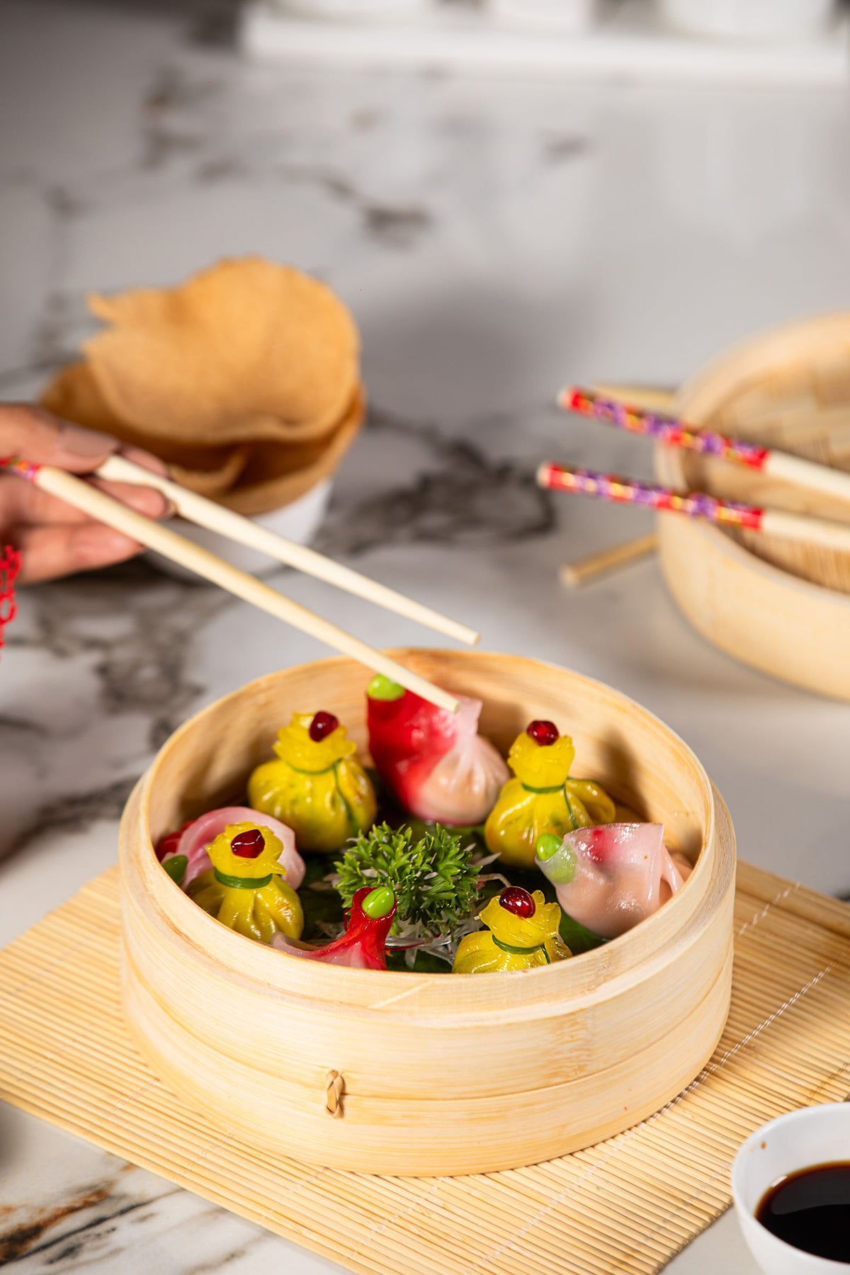 Colourful assorted dumplings in a bamboo steamer with chopsticks ready to pick one up