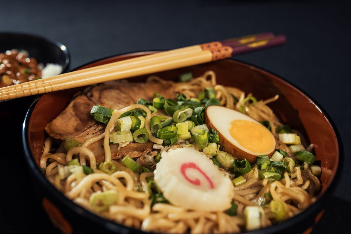 A bowl of Japanese ramen with boiled egg, scallions and narutomaki fish cake served with chopsticks
