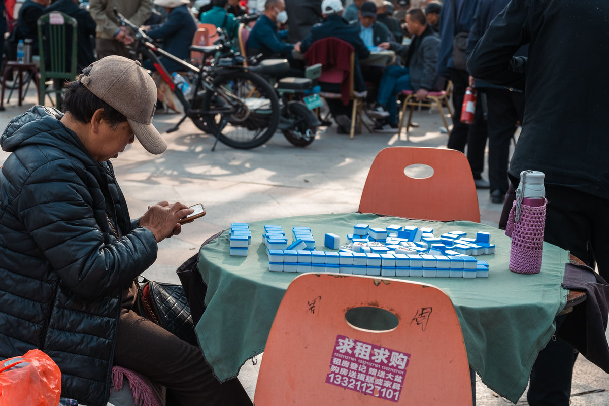People playing mahjong outdoors in a park with tiles arranged on a table