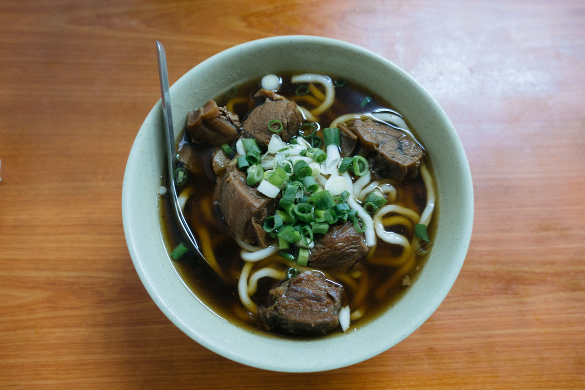 Steaming bowl of beef brisket noodle soup with green onions and dark broth
