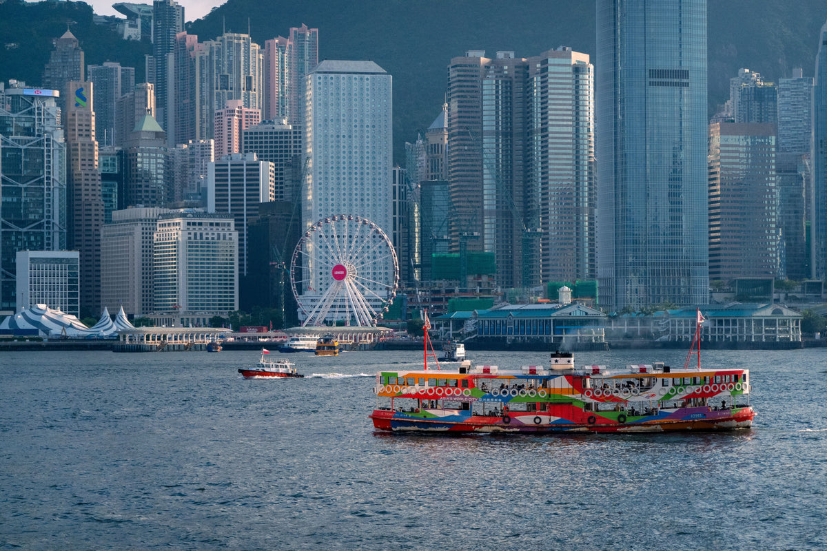 Colorful Star Ferry crossing Victoria Harbour with Hong Kong skyline and Ferris wheel in background