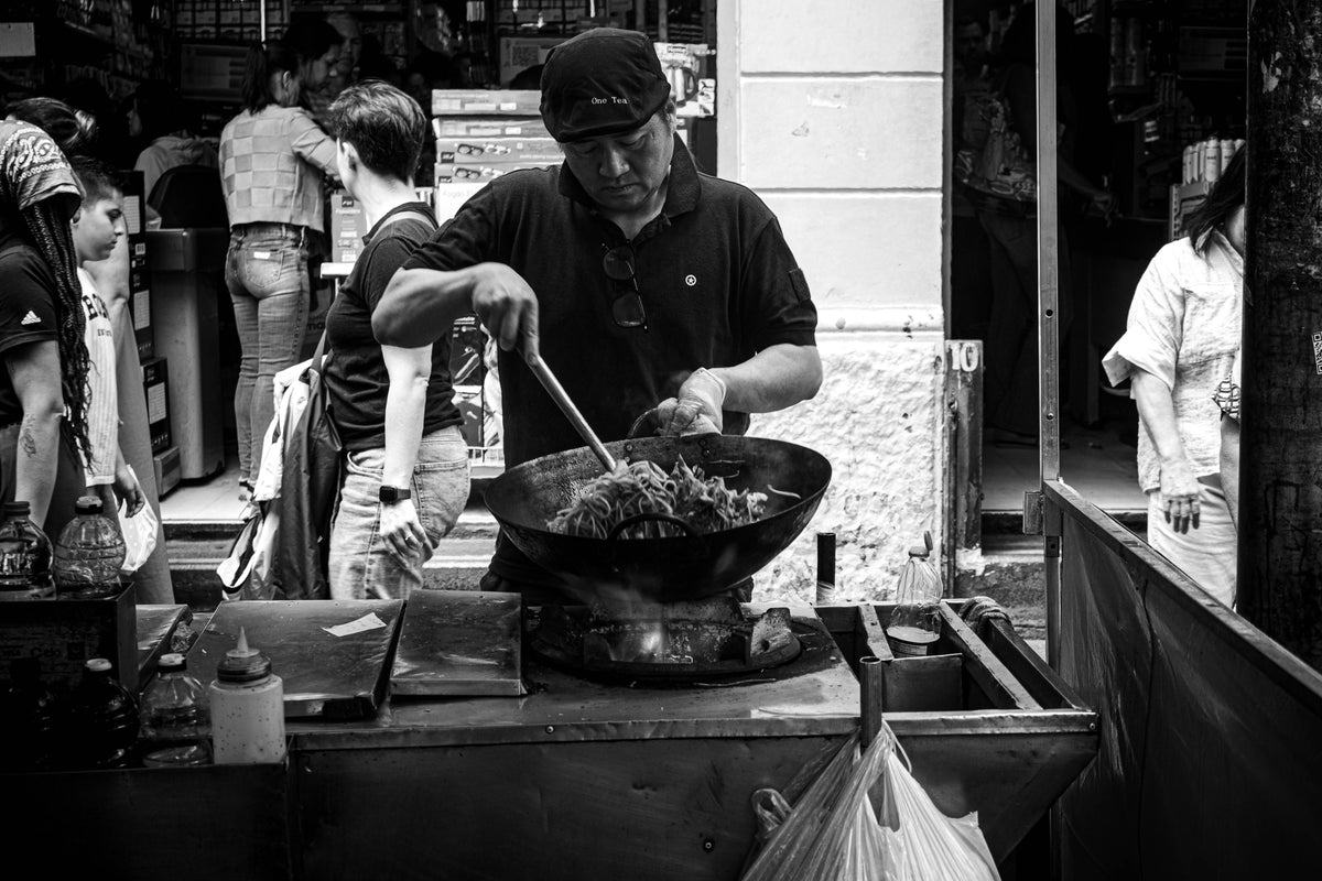 Street food vendor cooking noodles in a wok at a busy outdoor dai pai dong