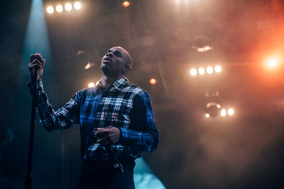 Singer holding a microphone under bright stage lights during a live concert
