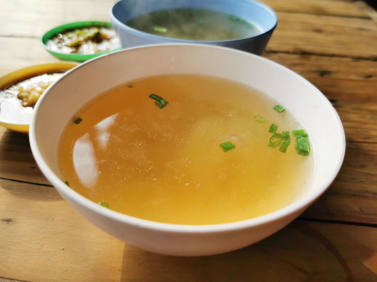 Warm bowl of soup topped with green scallions on a rustic wooden table