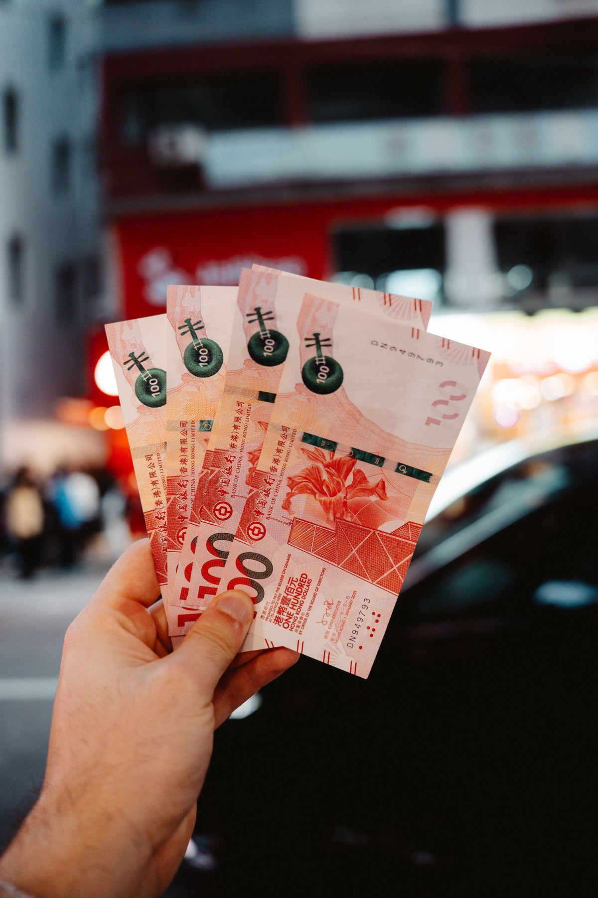 Hand holding Hong Kong dollar banknotes against a vibrant city background at night