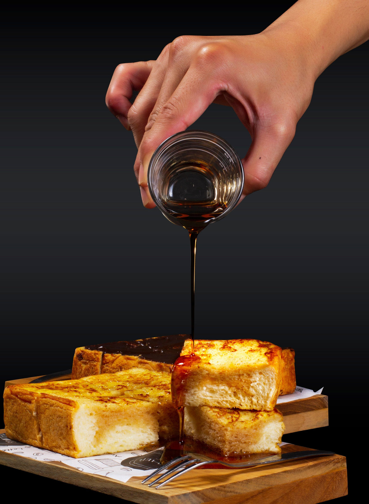 Golden French toast with syrup being poured over it on a black background