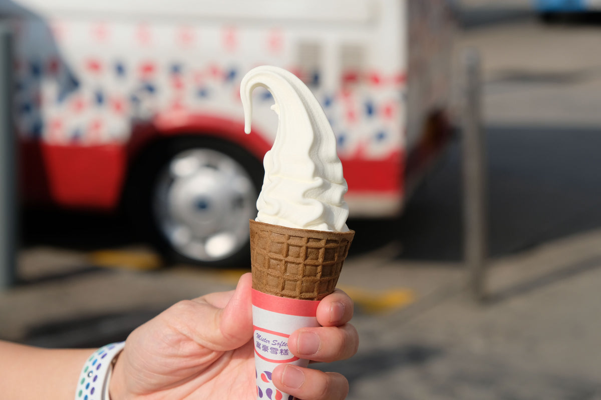 A vanilla soft serve cone held in front of a Hong Kong ice cream truck