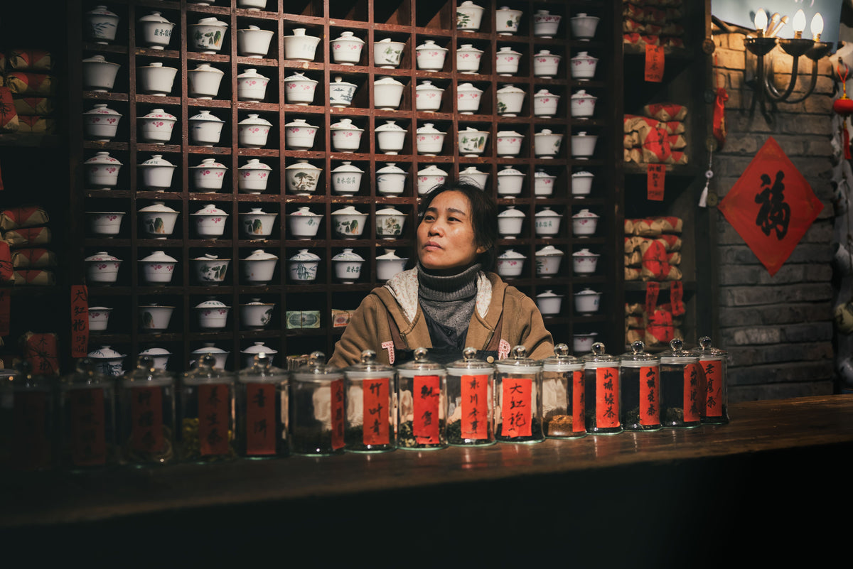Traditional Chinese teahouse interior with attendant surrounded by tea jars and teacups