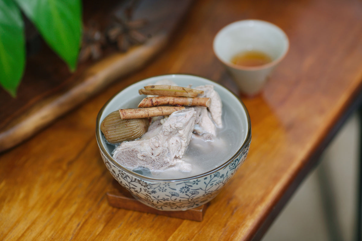 Cantonese herbal soup with meat served on a wooden table with a cup of tea