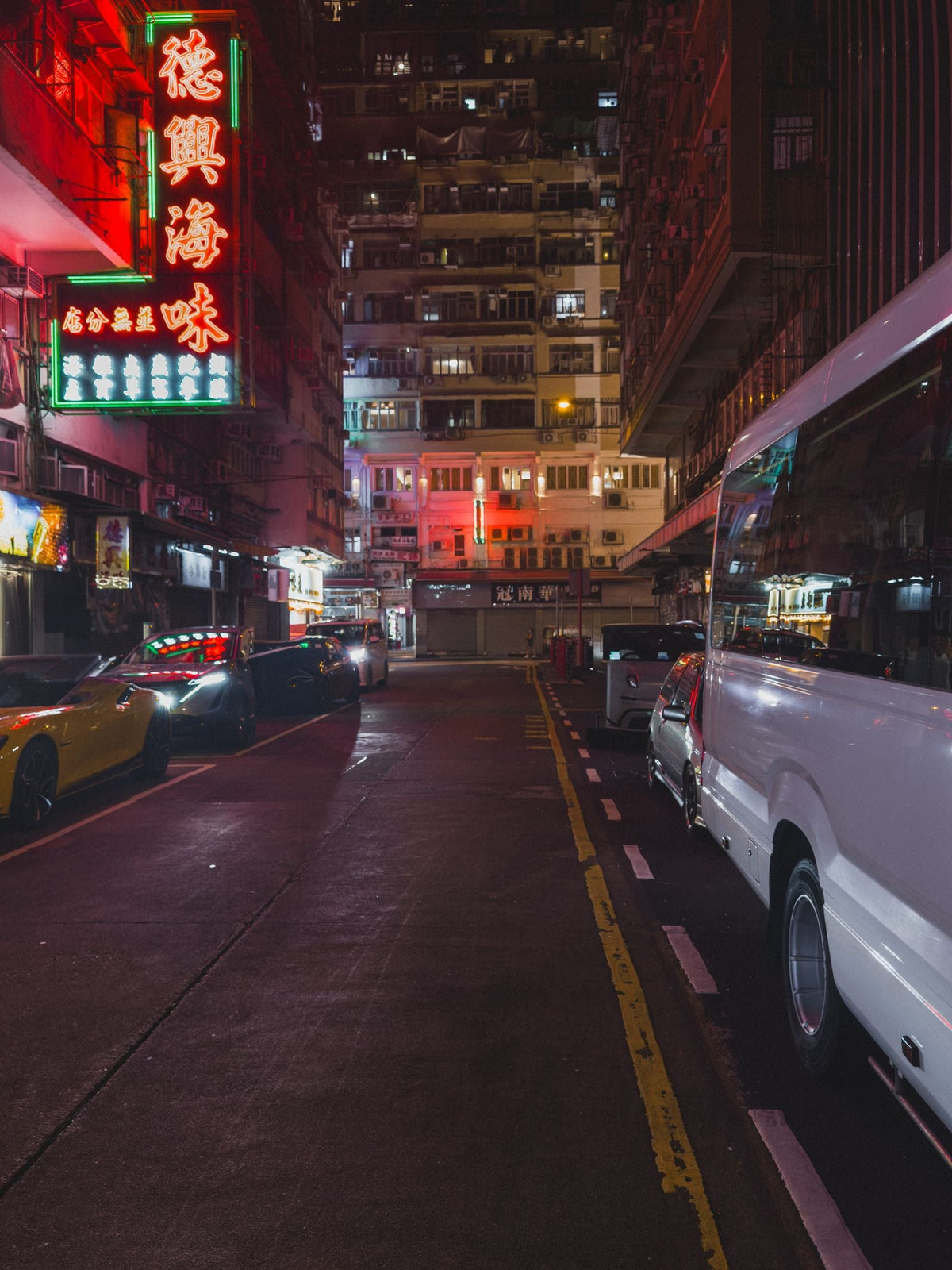 Moody Hong Kong night street with neon lights and parked cars