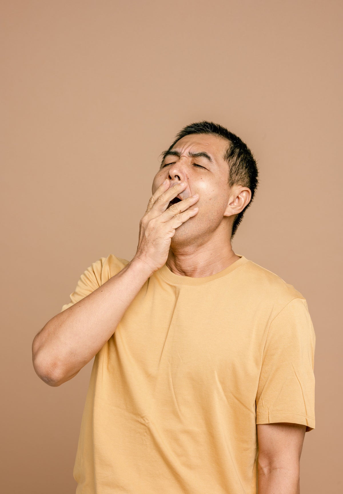 A young Asian man yawning with hand over mouth, expressing tiredness