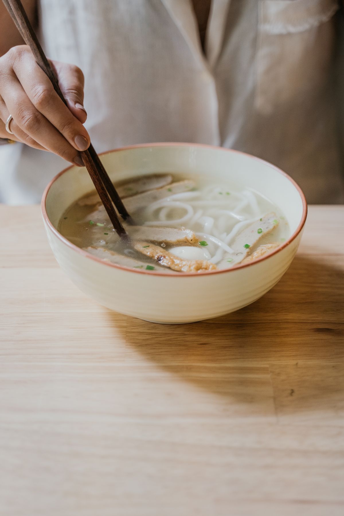 Close-up of chopsticks lifting rice noodles from a bowl of hot Asian soup