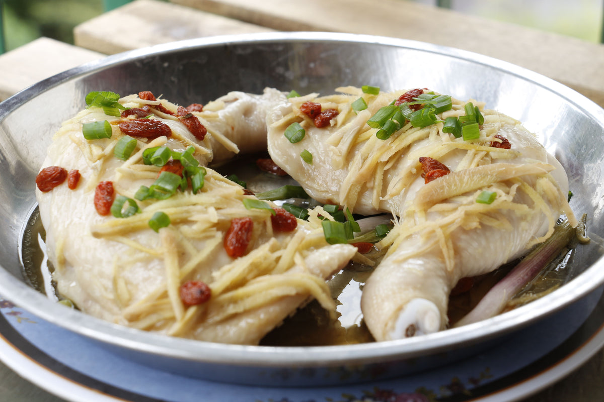 Cantonese-style steamed chicken garnished with ginger and scallions in a bowl