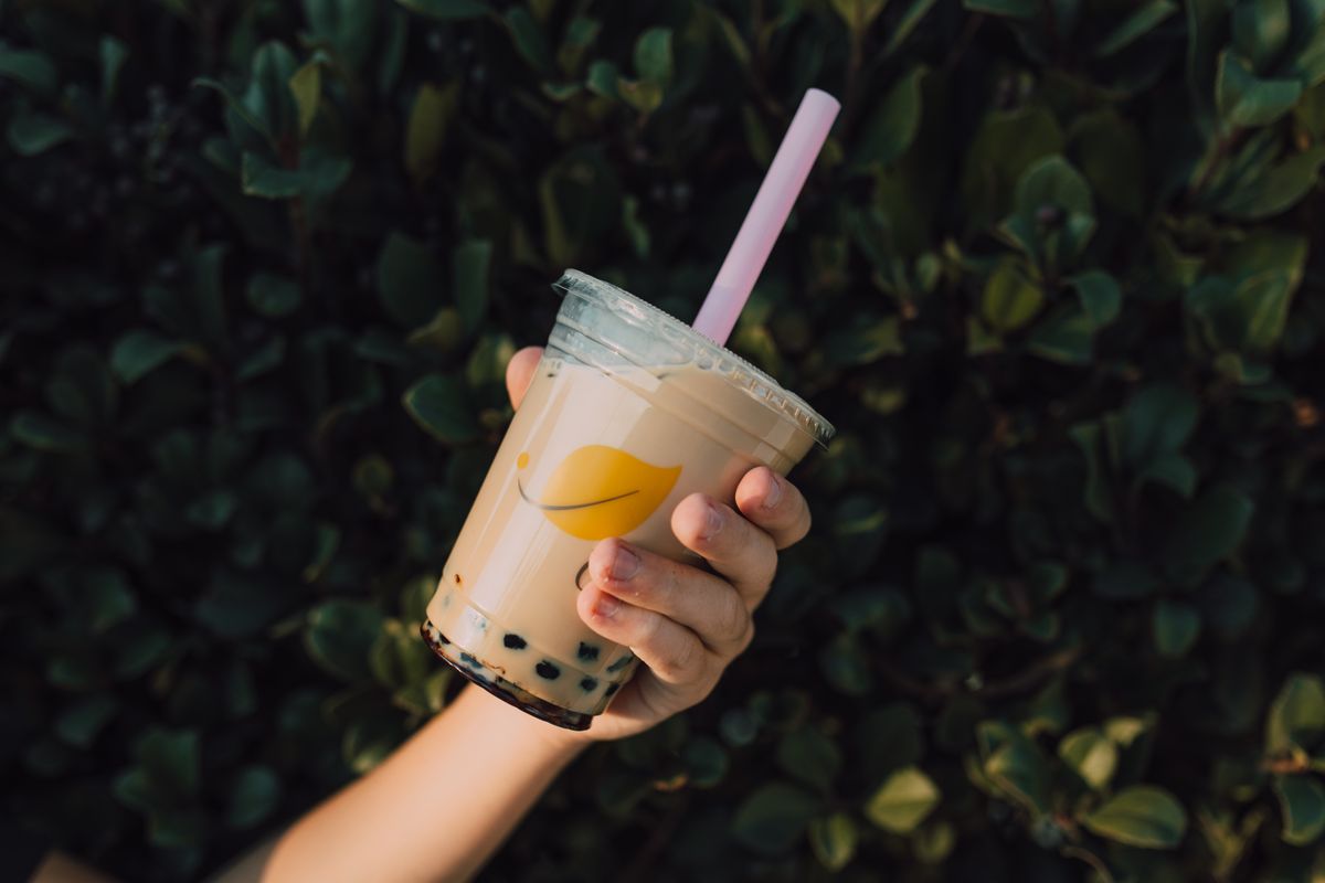 A hand holding a cup of iced milk tea in a plastic takeaway cup