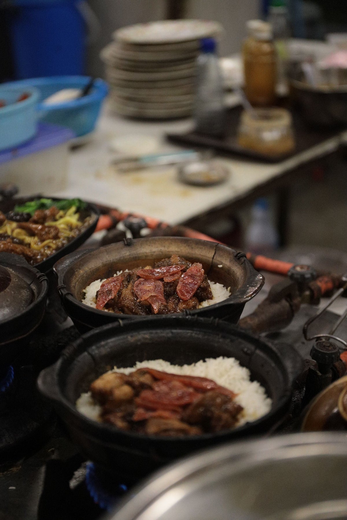 Clay pot rice with sausage and vegetables shown in a busy kitchen