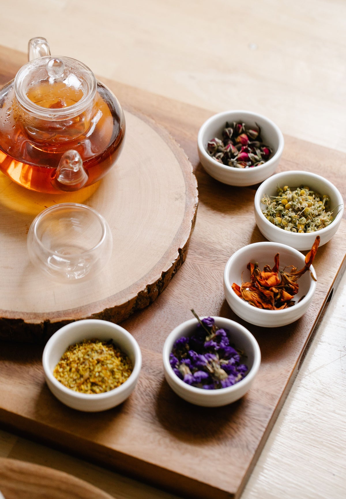 Glass teapot with herbal tea and assorted dried herbs in bowls on wooden surface