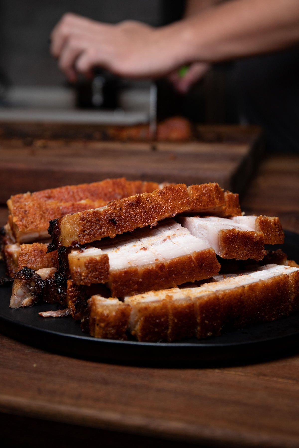 Cantonese crispy roast pork belly on a black plate showing crackling skin — Siu Yuk