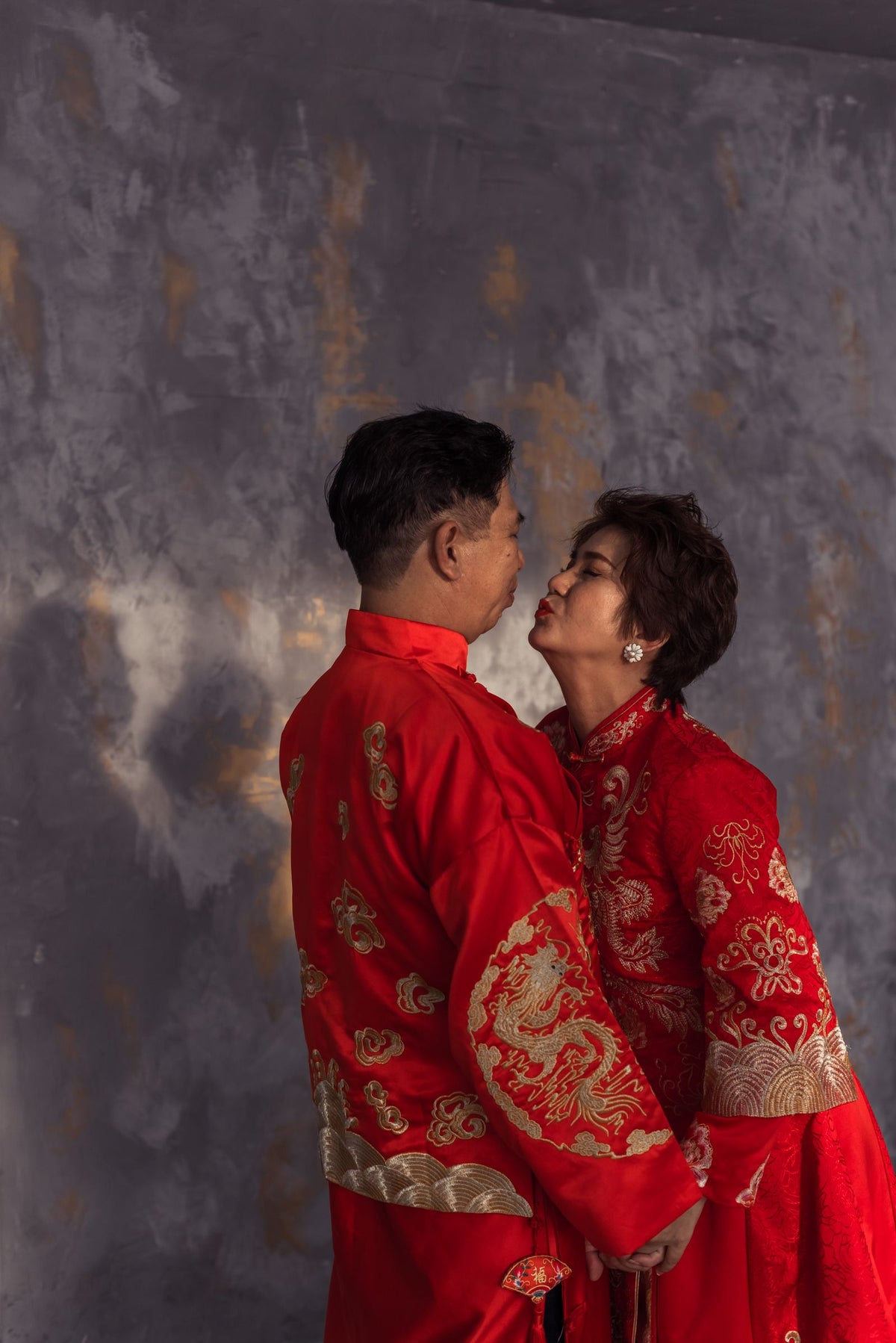 A couple in elegant red traditional Chinese wedding clothing sharing a private moment indoors