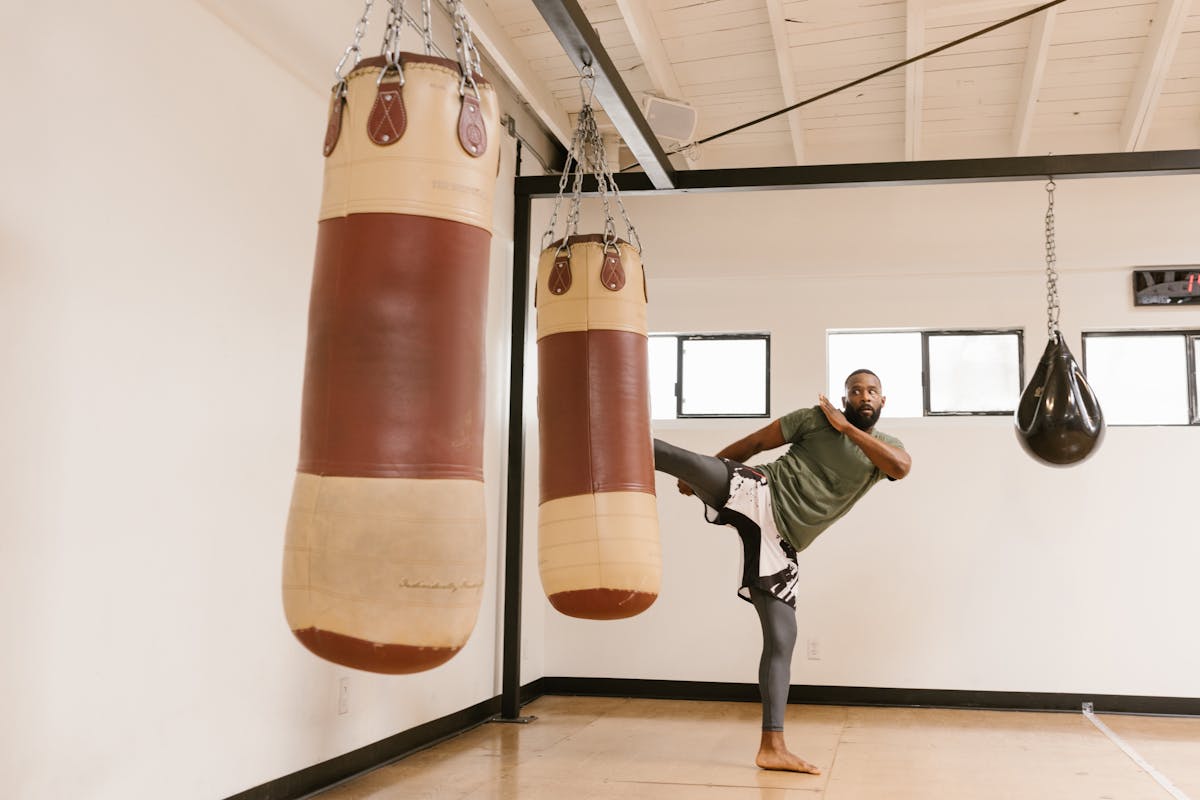 A man performing a high kick against a punching bag in a gym