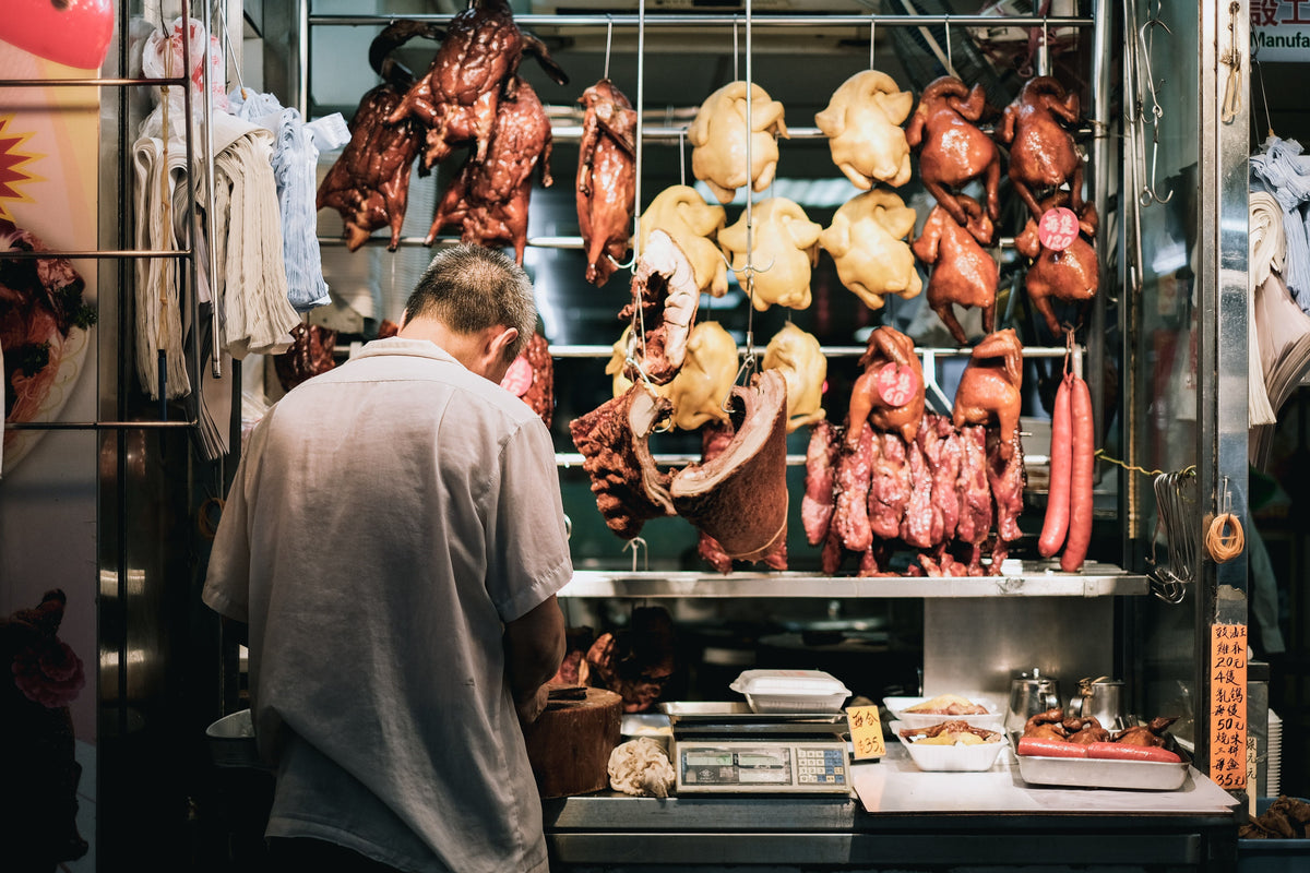 Cantonese wet market butcher preparing hanging meats behind a stall